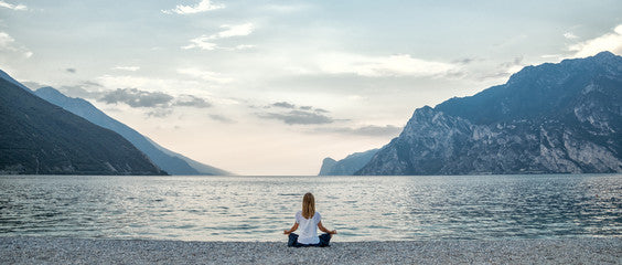 Person meditating on a beach with mountains and lake in the background
